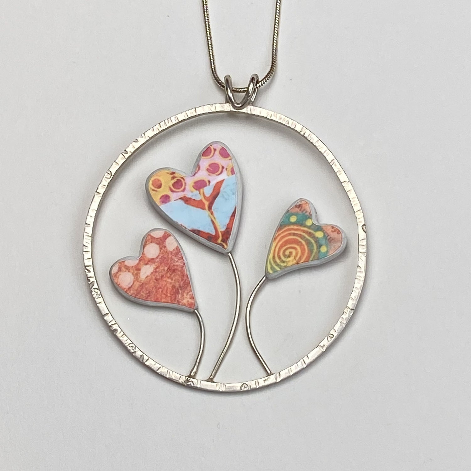 Three heart shaped flowers with bright prints grow in a textured ring of silver